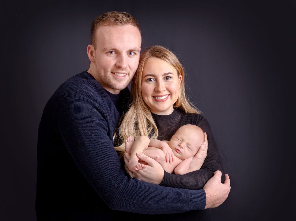 Portrait of new parents holding their sleeping newborn baby