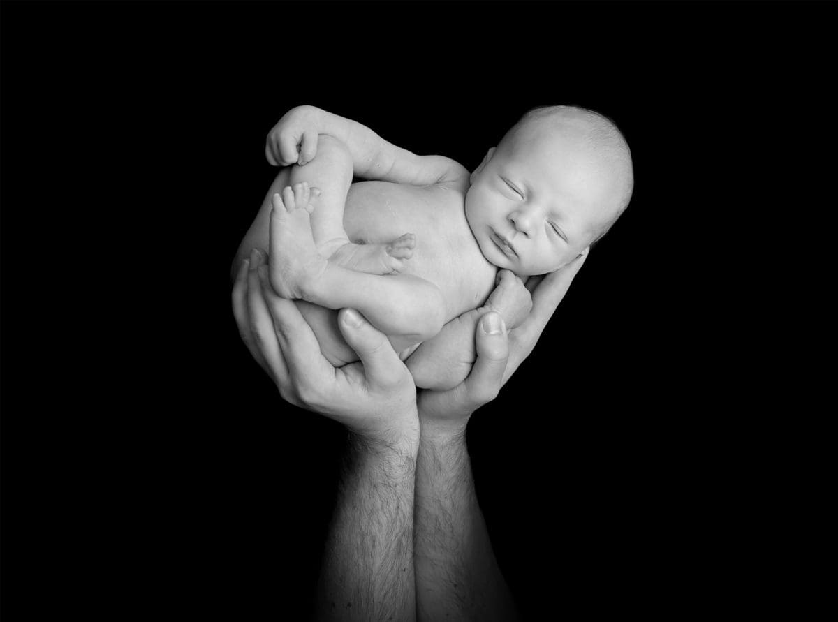 Black and white photograph of newborn baby held aloft in father’s hands