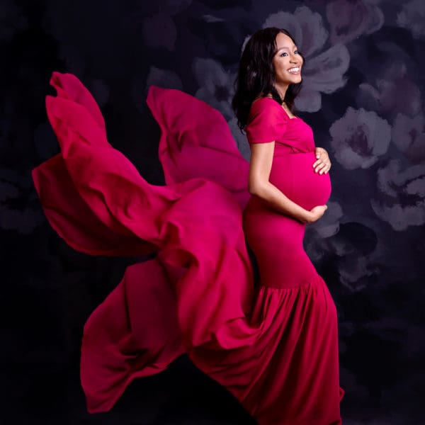 Pregnant mum-to-be showing off baby bump wearing a red floaty dress in maternity portrait