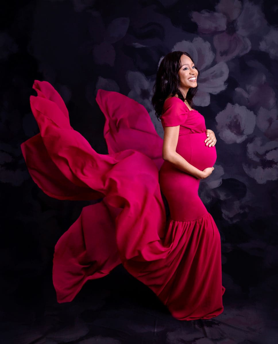 Pregnant mum-to-be showing off baby bump wearing a red floaty dress in maternity portrait