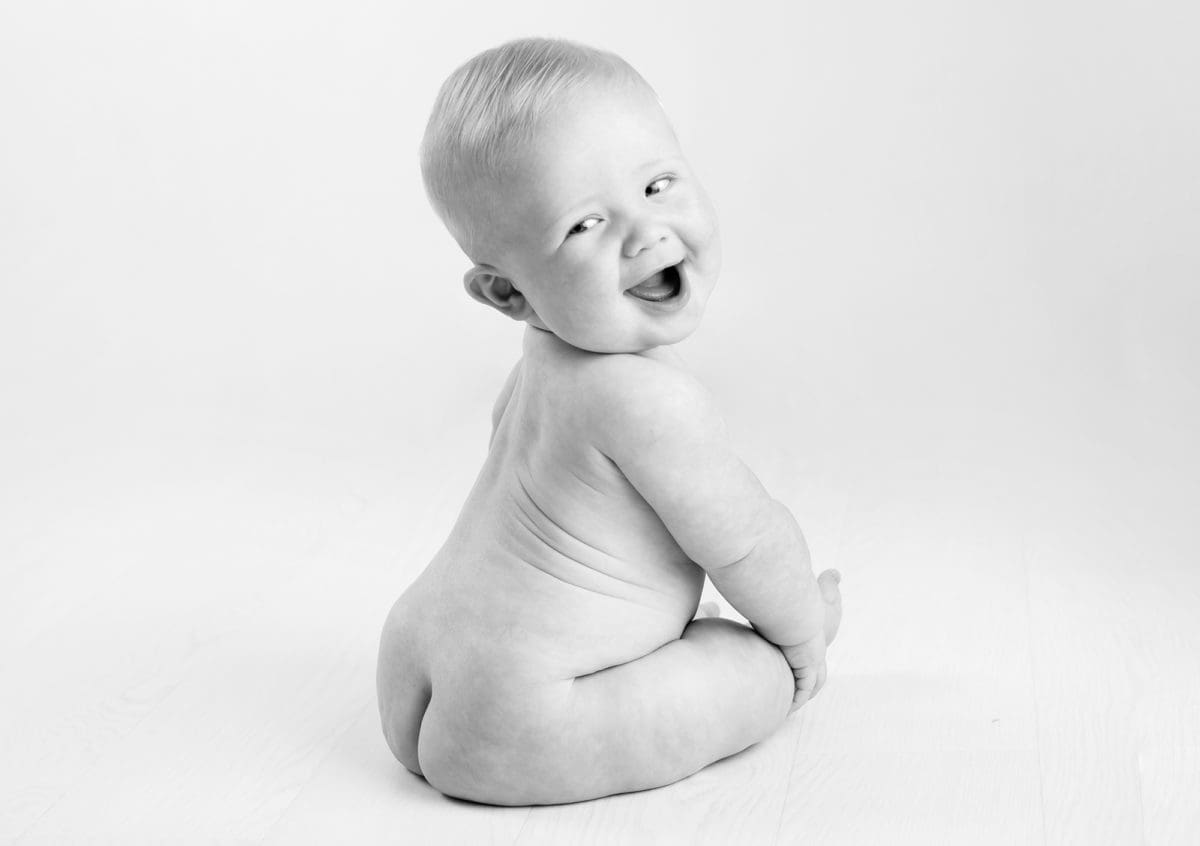 Cheeky baby in black and white baby photography session smiling while looking back over shoulder