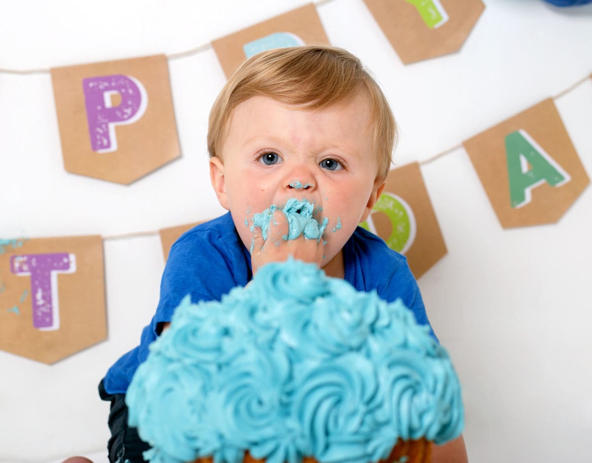 Baby boy portrait of cake smash photo session stuffing cake into mouth