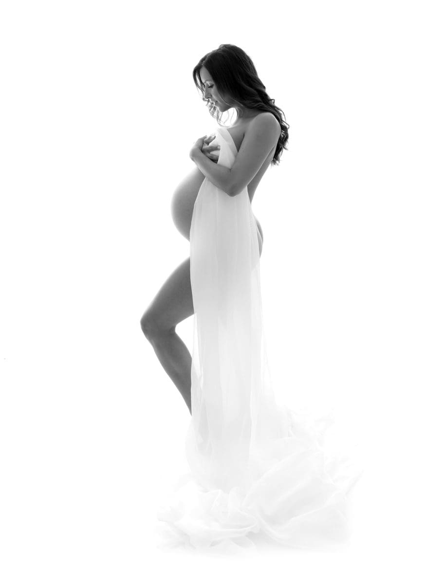 High key black and white pregnancy photo in which girl lovingly shows her baby bump