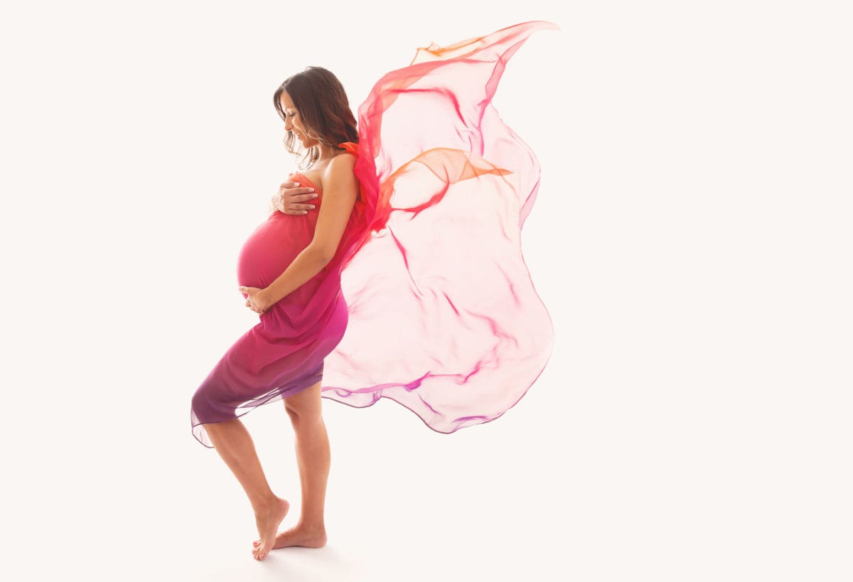 High key maternity portrait photography with pregnant lady showing baby bump and shrouded in floaty pink gossamer wrap