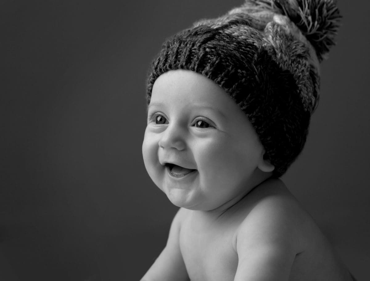 Black and white baby portrait of beautiful smiling baby wearing a wooly bobble hat