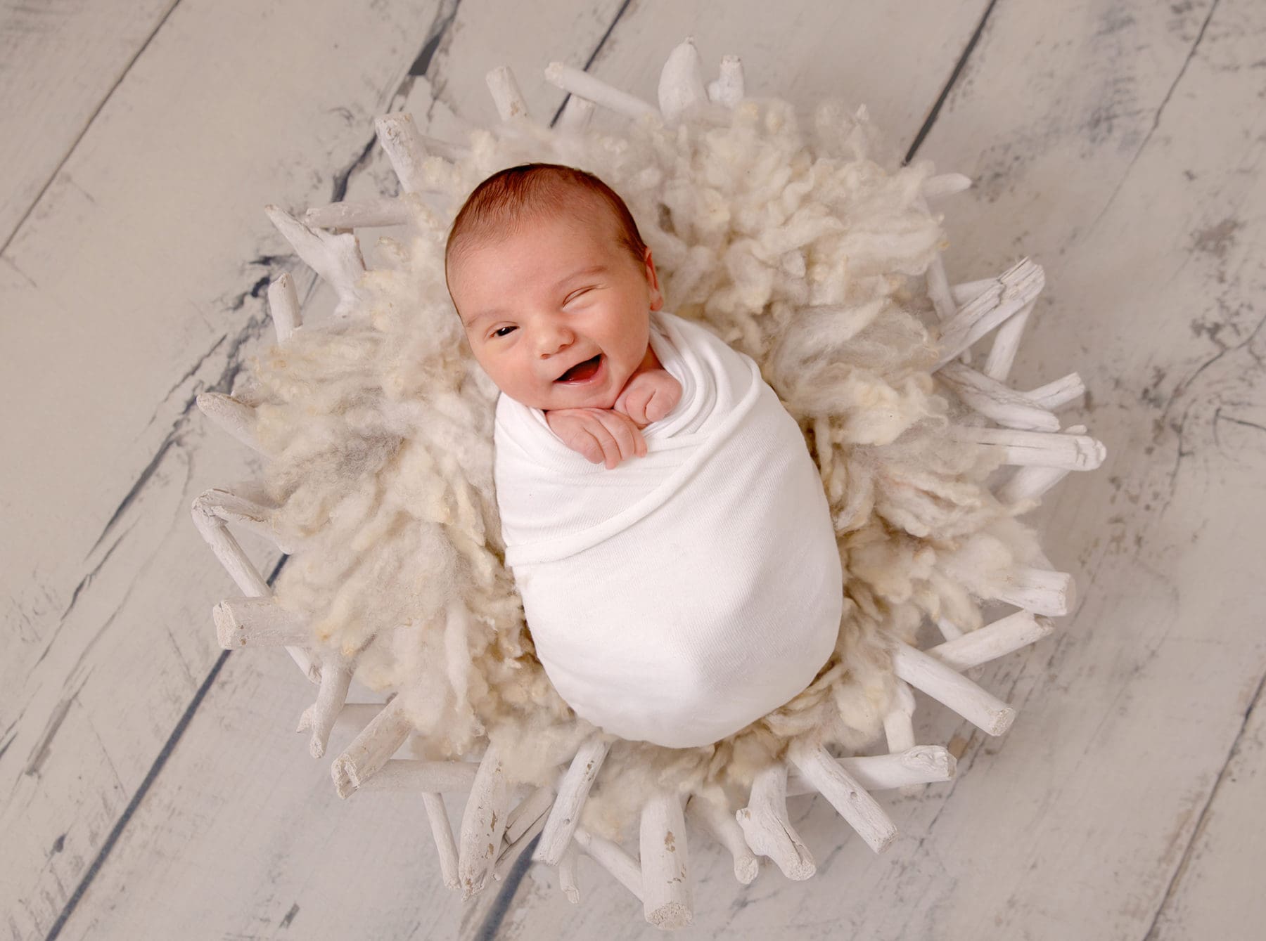 Photograph of smiling newborn baby swaddled and giving a cheeky wink