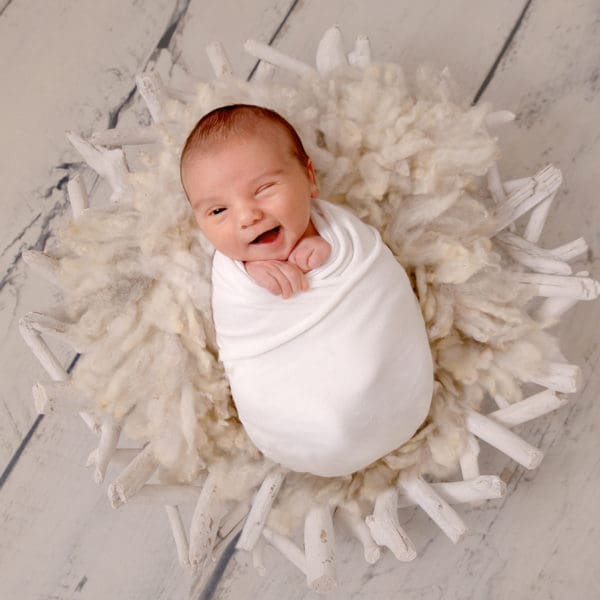 Photograph of smiling newborn baby swaddled and giving a cheeky wink